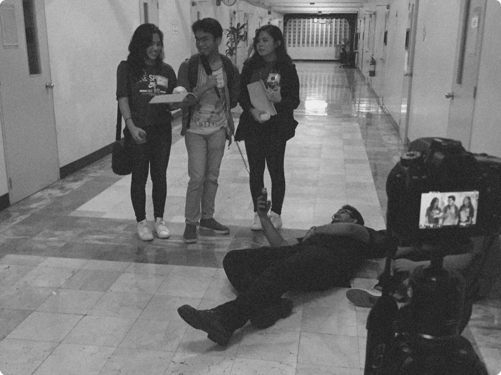 Uzair lying on a hallway floor holding a microphone up for three people on camera